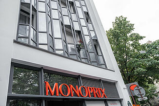 Façade of a residential and commercial building in Paris with a Monoprix supermarket on the ground floor and flats above.