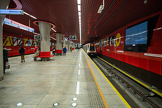 Metro station in Warsaw with red walls next to the tracks and red benches in the waiting area.
