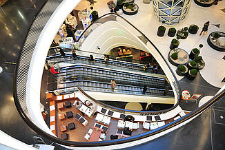 Interior view of the Palais Quartier in Frankfurt with seating areas, shops, escalators and plants. 