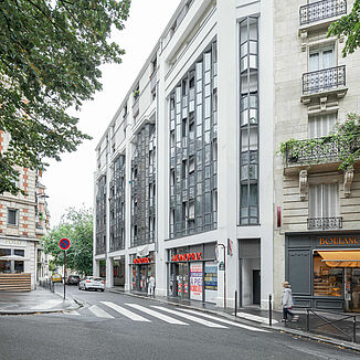 Exterior view of a residential and commercial building in Paris, with a Monoprix supermarket below and flats above