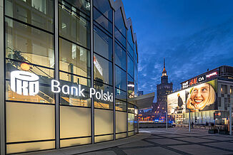 The illuminated Bank Polski in the Rotunda mixed-use building and other commercial buildings in Warsaw at night.