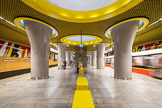 Waiting area with yellow colour accents on walls, ceilings and lamps in a metro station in Warsaw.