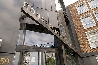 Entrance to a modern building with a black façade, which houses the Léo Délibes music school in Paris.