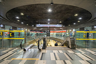 Metro station in Warsaw with escalators and various shops.