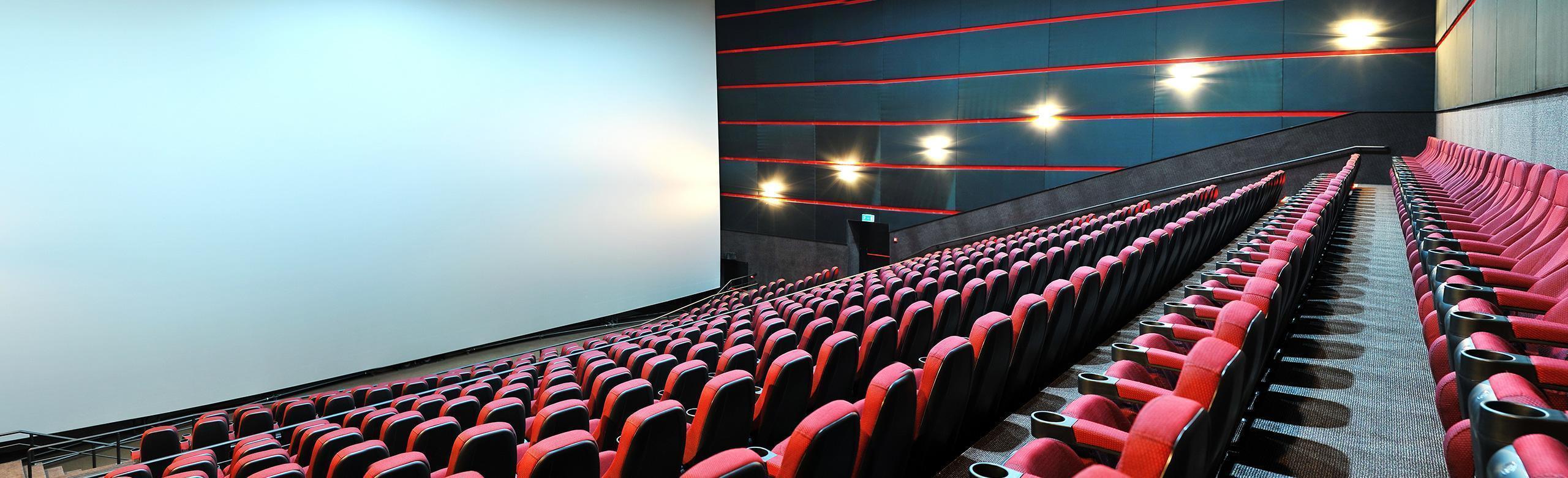 cinema acoustic solutions A large cinema hall with red armchairs and a big screen.